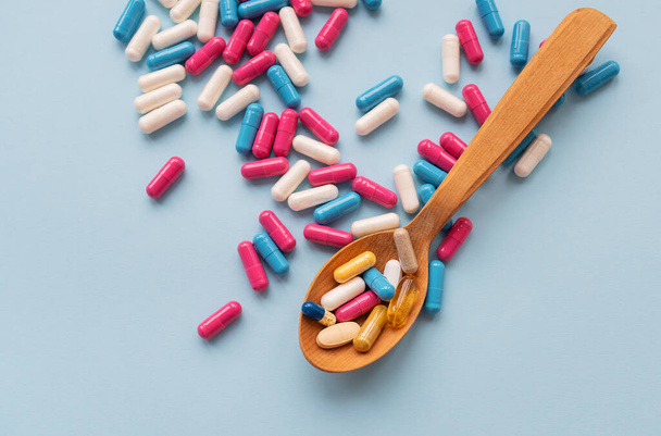 Varie pillole luminose su uno sfondo blu si trovano in un cucchiaio di legno sullo sfondo di diverse pillole luminose. Concetto sanitario - Foto, immagini