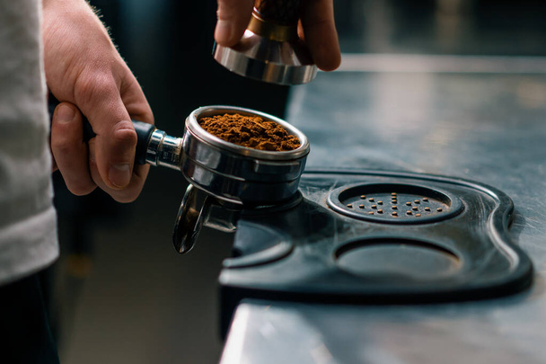 A professional barista in coffee shop prepares ground coffee by tamping fresh ground coffee beans close-up - Foto, imagen