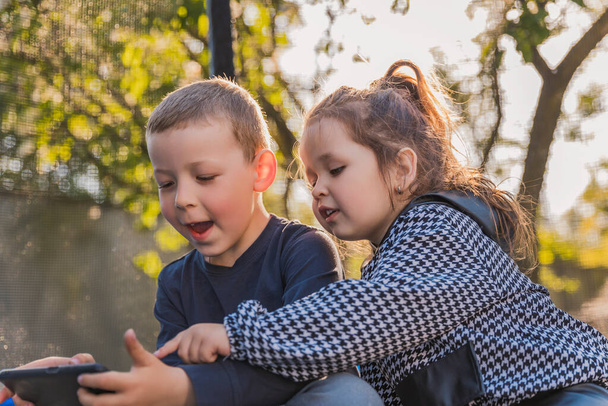 portrait of children who sit on a trampoline and look at the phone - Foto, Imagem