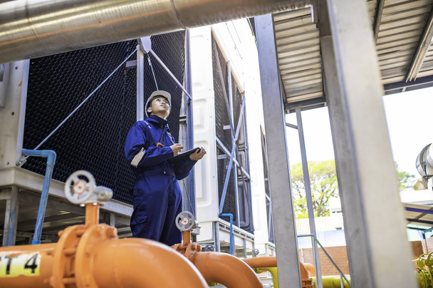Mladý inženýr pracující ve velké továrně, technik v ochranné uniformě a s kontrolou teploty v potrubí - Fotografie, Obrázek