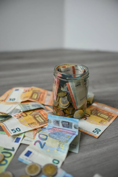 Putting money into the jar, lots of Euro coins and banknotes - Фото, изображение