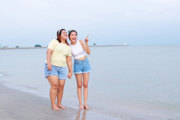 Dos chicas asiáticas gordas y delgadas viajan por el mar de vacaciones. Párate y observa el mar en la playa. Mujer viajera. Concepto de viaje y estilo de vida. espacio de copia - Foto, Imagen