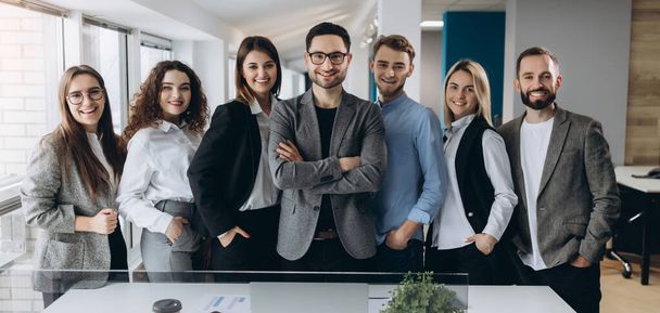 Portret van een lachende groep uiteenlopende corporate collega's staan in een rij samen in een lichte moderne kantoor - Foto, afbeelding