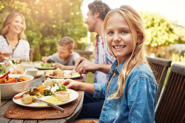 We make sure to make time for our family. Portrait of a happy little girl enjoying an outdoor lunch with her family - Foto, imagen