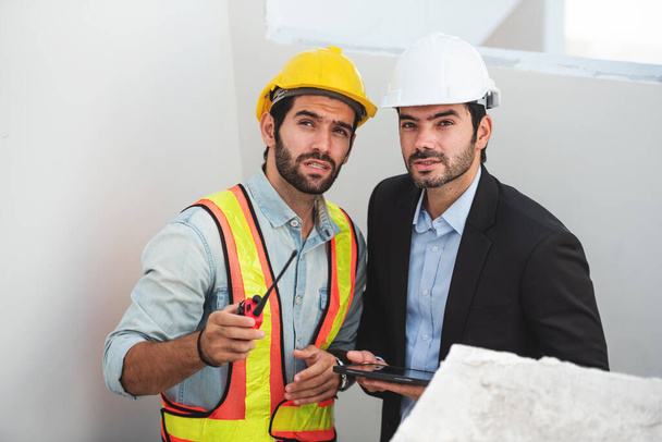 Csapatmunkások az építkezésen, két építőmérnök sisak keménykalapban, digitális táblagéppel és tervrajzzal, miközben a gyárban állnak.. - Fotó, kép