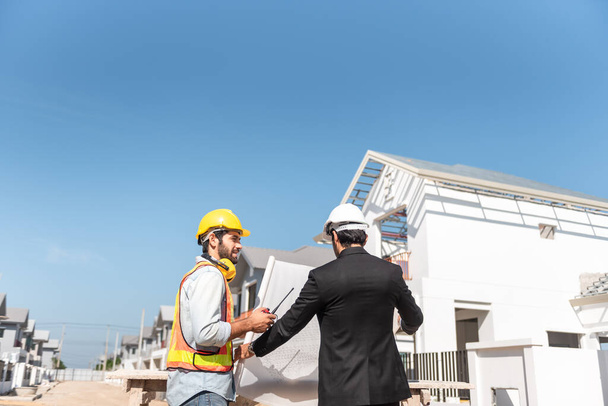 Hombres de trabajo en equipo en el sitio de construcción, dos ingenieros civiles en casco de seguridad casco duro usando tableta digital y plano de trabajo mientras están de pie en la fábrica. - Foto, Imagen