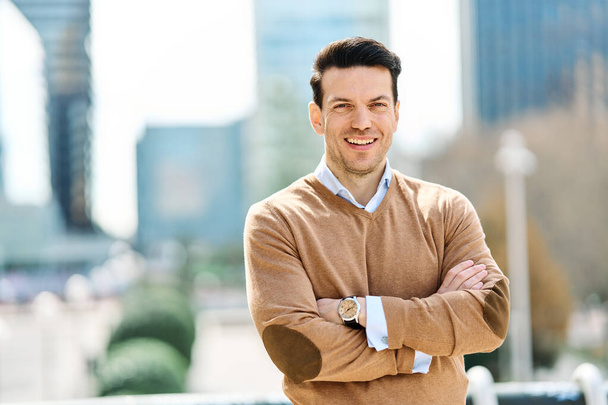 Портрет молодого бізнесмена, який посміхається в камеру, що стоїть з обіймами, схрещеними на відкритому повітрі
 - Фото, зображення
