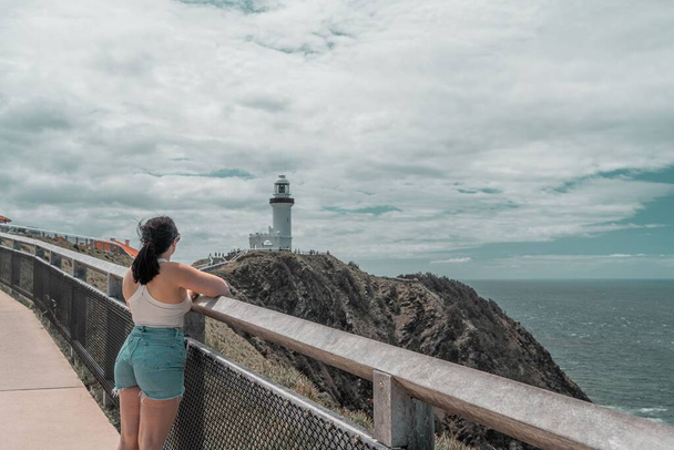 A woman looking at the white lighthouse at the coast of Byron Bay - 写真・画像