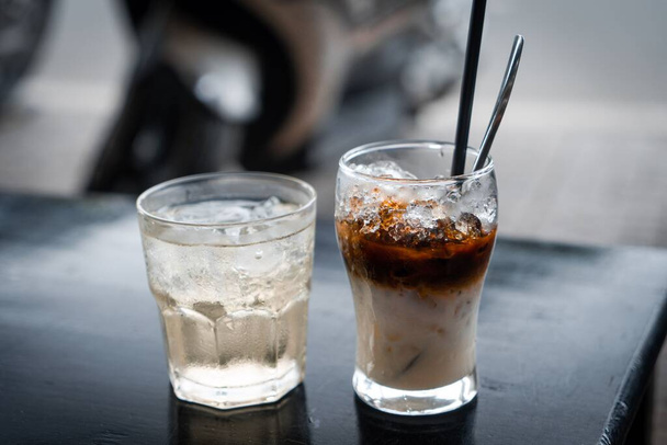 An iced water and an iced coffee in glasses on a black table - Фото, зображення
