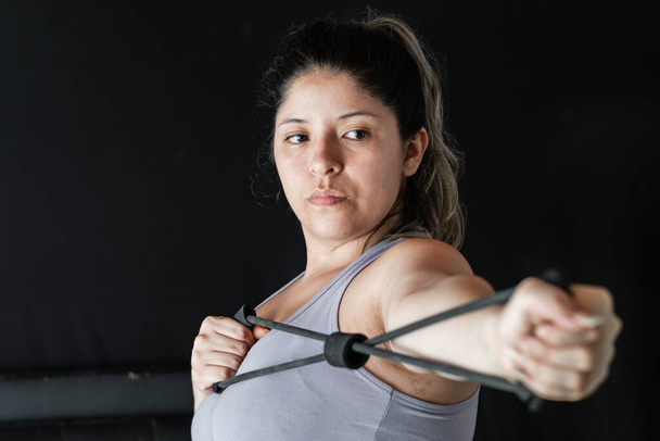 close-up of a young latina woman stretching an elastic band with her hands to exercise her muscles. - Foto, Bild