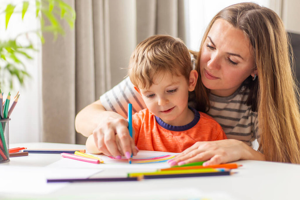 Rysunek matki i dziecka z ołówkami siedzącymi przy biurku w domu. Szczęśliwa rodzina - Zdjęcie, obraz