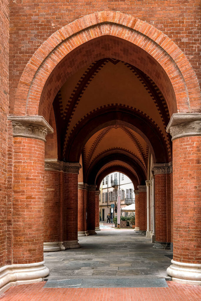 Passage through red brick walls and columns under vaulted ceiling in old town of Alba, Italy (vertical composition). - Foto, Bild