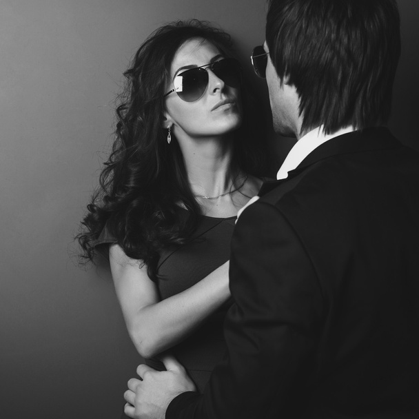 Splendida ragazza in occhiali accanto al muro e il suo uomo di fronte a lei. Bianco nero
 - Foto, immagini
