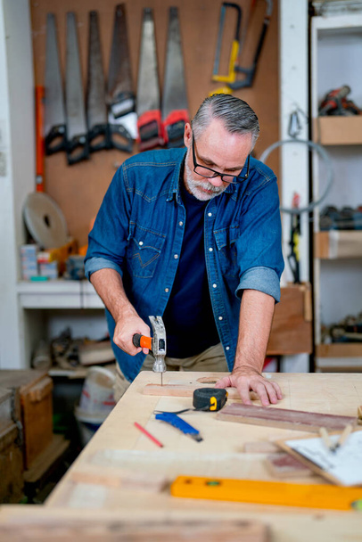 homme charpentier caucasien utiliser marteau pour frapper ongle sur table en bois pour le travail dans le lieu de travail. - Photo, image