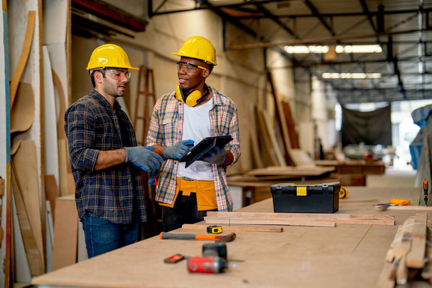 Afro-américain et homme de charpentier caucasien discuter ensemble sur le travail du bois en utilisant la tablette dans le lieu de travail de l'usine. - Photo, image