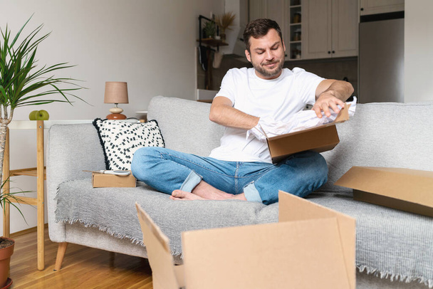 Man sitting on sofa and unboxing postal parcel. - Photo, Image