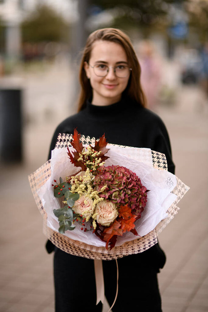 Young woman holding big and beautiful autumn style bouquet of fresh roses, hydrangea , dog-rose, gypsophila and oak leaves - Foto, afbeelding