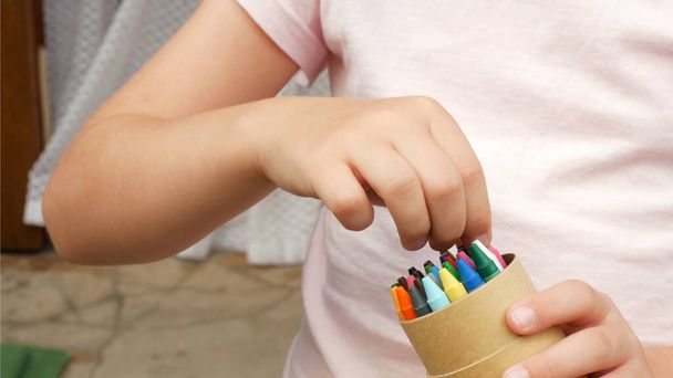 Niño anónimo, niña en edad escolar sosteniendo una caja de crayones eligiendo un crayón detalle manos primer plano, creatividad artes y manualidades arte educación concepto abstracto, símbolo, una persona. Niños y creación de arte - Foto, Imagen