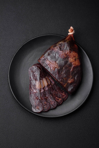 Köstliche geräucherte oder gepökelte Mahan-Pferdefleischwurst mit Gewürzen und Kräutern auf dunklem Betongrund - Foto, Bild