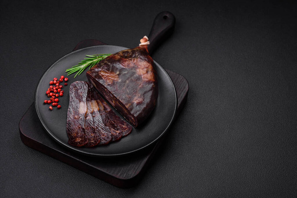 Вкусная копченая или излеченная колбаса из конины махан со специями и травами на темном бетонном фоне - Фото, изображение