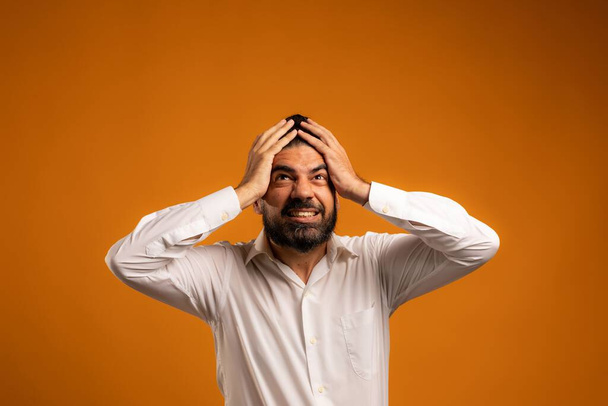 A beautiful shot of a Hispanic man showing emotions in front of an orange background - 写真・画像