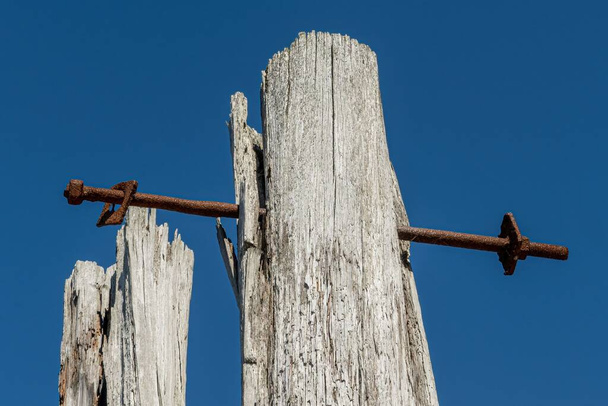 A low angle shot of rusty metal pole into old weathered wooden fence post on blue sky background - 写真・画像