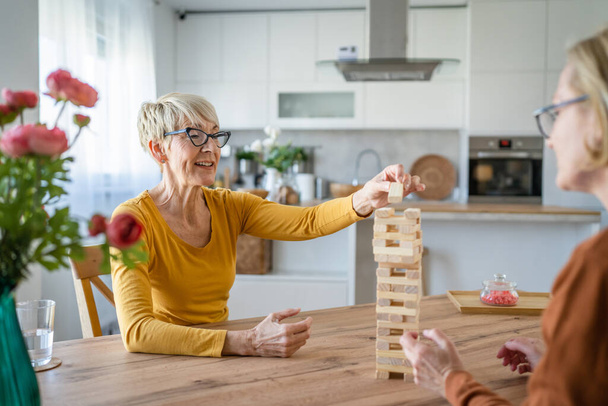 twee senior vrouwen vrouw vrienden of familie zussen spelen vrijetijdsbesteding bordspel thuis veel plezier gepensioneerde grootmoeder tijd doorbrengen samen met hun volwassen dochter - Foto, afbeelding