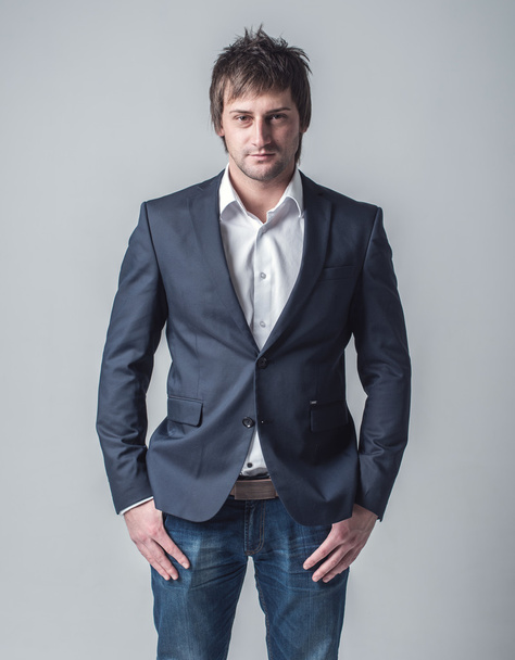 Jeune homme confiant vêtements formels veste classique et jean fond gris
. - Photo, image
