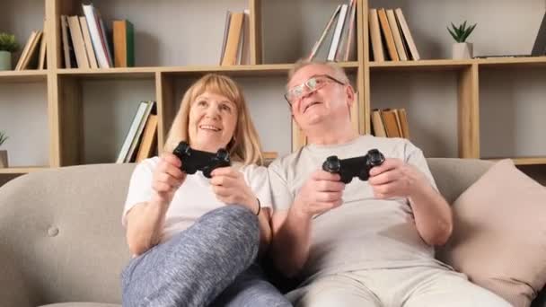 Oyun oynayan çok pozitif yaşlı bir çift bir joystick kullanıyor. Büyükbabalar oturma odasında otururken video oyunları oynarlar. Oyunu kazanmak için. Zaferin mutluluğu - Video, Çekim