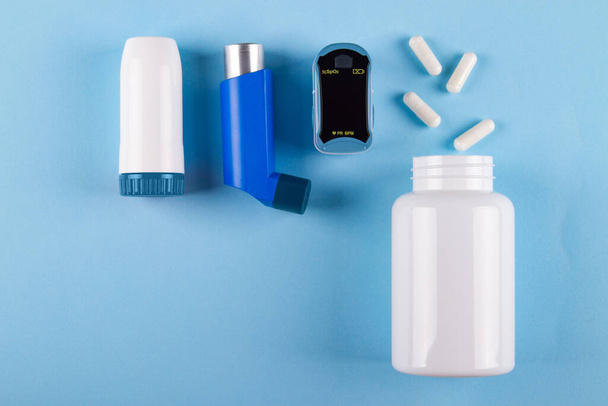 Bovenaanzicht van oximeter, fles pillen en inhalatoren op blauwe achtergrond met kopieerruimte. Concept van bronchiale irritatie veroorzaakt door astma - Foto, afbeelding