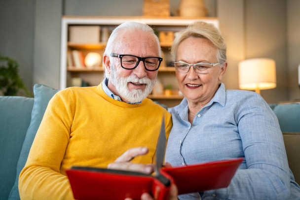 Vanhempi pari mies ja nainen aviomies vaimo etsii perhekuvia albumi valkoihoinen vanha mies ja nainen isoisä ja isoäiti onnellinen hymy kotona vanhoja kuvia oikeita ihmisiä kopioi tilaa - Valokuva, kuva