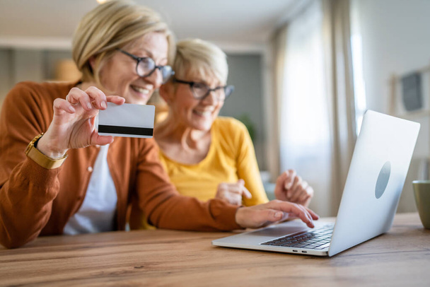 two mature senior women grandmother females sit at home use credit or debit card for online shopping browse internet stores buying stuff use digital tablet real people copy space - 写真・画像
