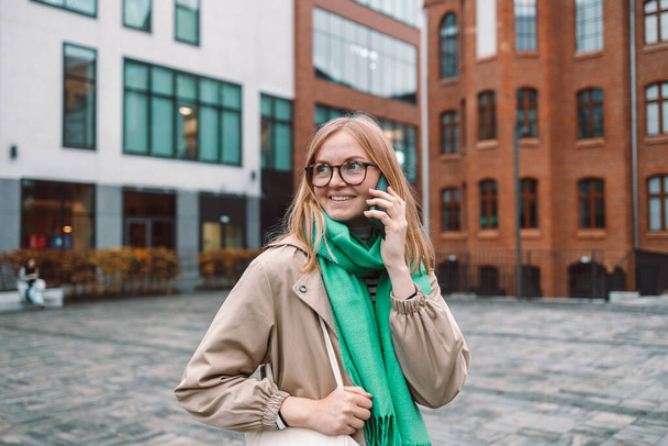 Hermosa mujer joven hablando en teléfono inteligente caminando por la calle de la ciudad. Retrato de una hermosa hembra sonriente usando teléfono móvil. Foto de alta calidad - Foto, imagen