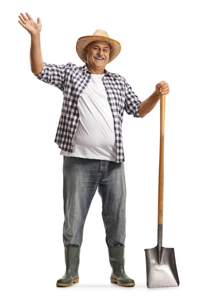 Retrato de comprimento total de um agricultor maduro feliz com uma pá acenando e sorrindo isolado em fundo branco - Foto, Imagem