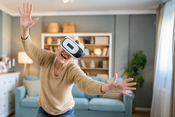 Una donna matura anziana caucasica femmina a casa godersi la realtà virtuale VR auricolare - Foto, immagini
