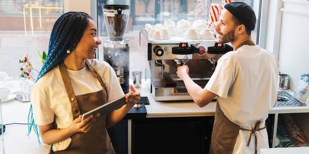Smiling male barista making coffee while talking with his female colleague. Young waitress using digital tablet. Online order concept - Foto, Imagem