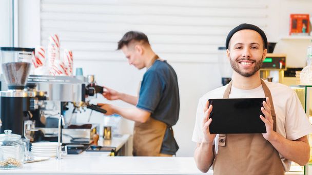 Happy stylish man working in coffee shop while holding tablet with empty screen. Copy space. Starting a small business - Valokuva, kuva