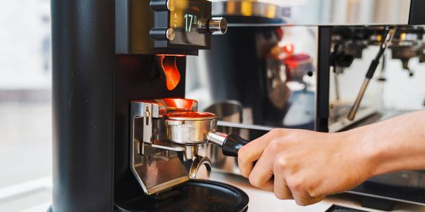 Close up of male barista using coffee grinder machine while making coffee in cafe. Preparation service concept - Zdjęcie, obraz