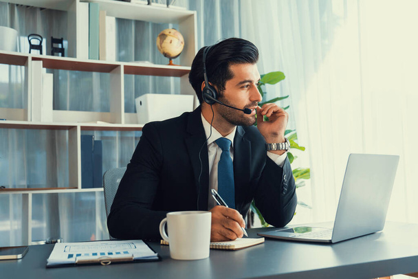 Mężczyzna operator call center lub przedstawiciel telesprzedaży siedzi przy biurku w słuchawkach i zajmuje się rozmową z klientem świadczącym obsługę klienta lub dokonującym sprzedaży. żarliwy - Zdjęcie, obraz