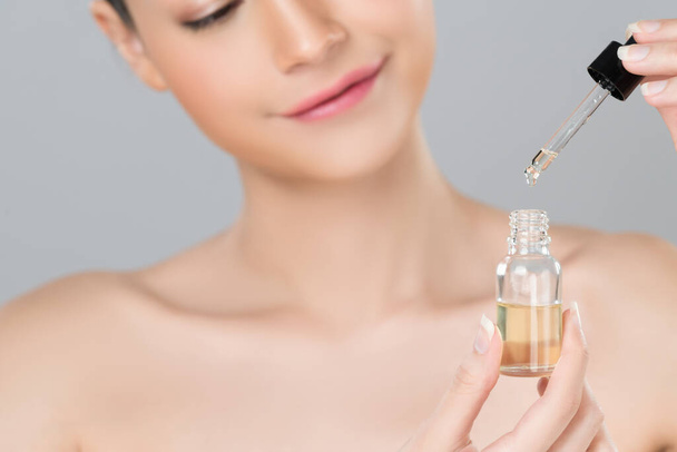 Focus cannabis extracted oil bottle with dropper lid holding by blurred glamorous beautiful asian woman with perfect clean skin and soft smooth makeup in isolated background. - Photo, Image