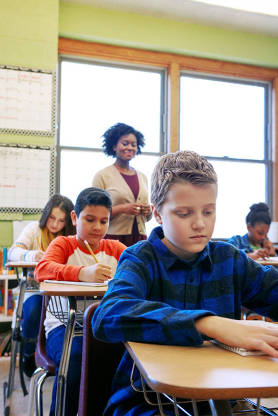 Assessment ist ein entscheidender Schritt im Lernprozess. ein kleiner Junge sitzt in der Klasse mit seinem Lehrer und Klassenkameraden im Hintergrund - Foto, Bild