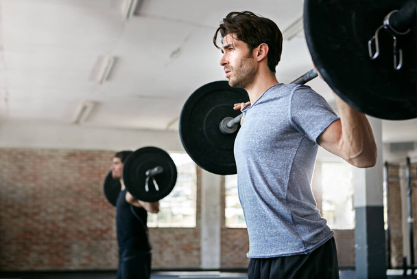 Empuja más fuerte, fortalécete. hombres jóvenes haciendo ejercicio con pesas en el gimnasio - Foto, Imagen