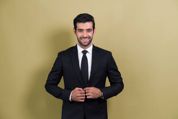 Elegante uomo d'affari in abito nero che posa con fiducia su sfondo isolato, con un sorriso felice e ottimista come successo e professionalità per l'uomo d'affari. Irritante - Foto, immagini