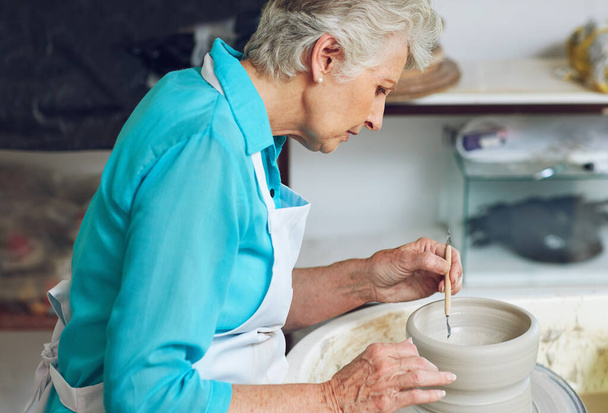 Spending time at the wheel. a senior woman making a ceramic pot in a workshop - 写真・画像