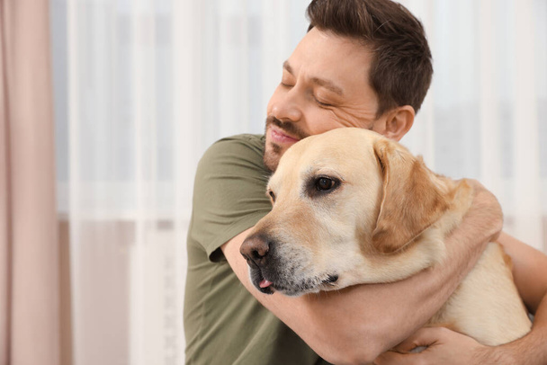 Man hugging his cute Labrador Retriever at home. Space for text - Foto, imagen