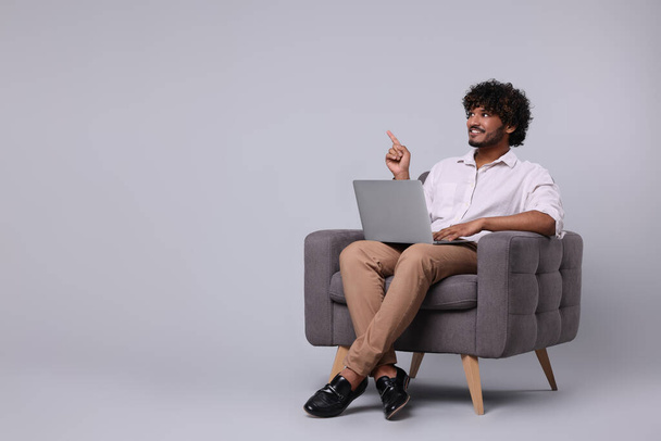 Smiling man with laptop sitting in armchair on light grey background, space for text - Foto, imagen