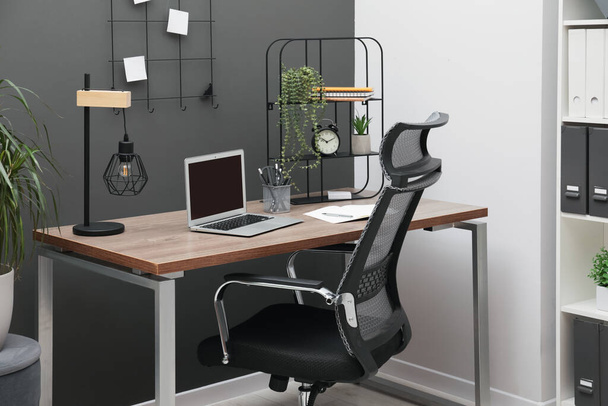 Przytulne miejsce pracy z nowoczesnym laptopem na biurku i wygodnym krzesłem w domu - Zdjęcie, obraz