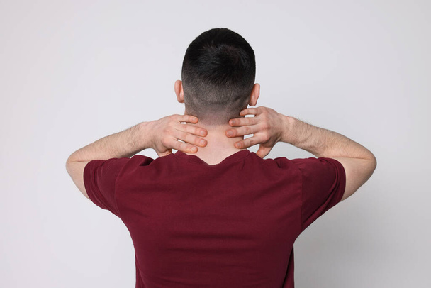 Man suffering from pain in his neck on light background, back view. Arthritis symptoms - Valokuva, kuva