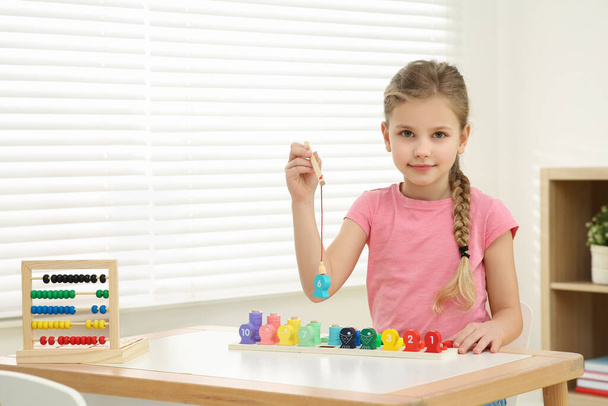 Little girl playing with Educational game Fishing for Numbers at desk in room. Learning mathematics with fun - Foto, Bild