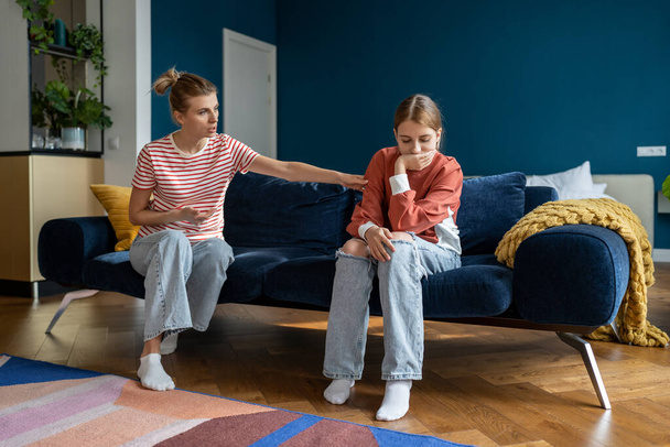 Young woman loving mother trying to speak with upset depressed teen daughter while sitting together on sofa at home, mom comforting teenage girl child, showing support. Anger in adolescents - Фото, зображення